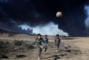 بچه ها به دنبال توپ درجنوب موصل در برابر چشم اندازی دود و نفت شعله ور شده